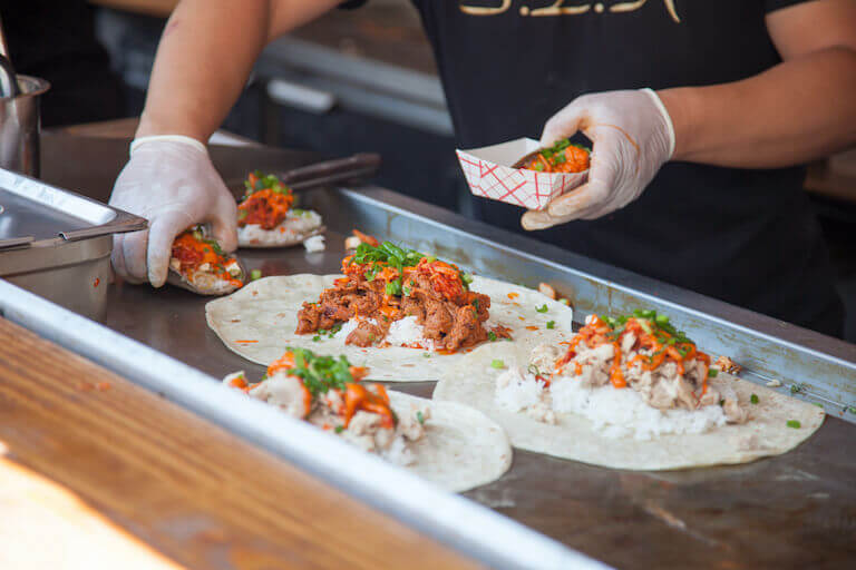 Employee wearing gloves putting tacos into a paper serving boat