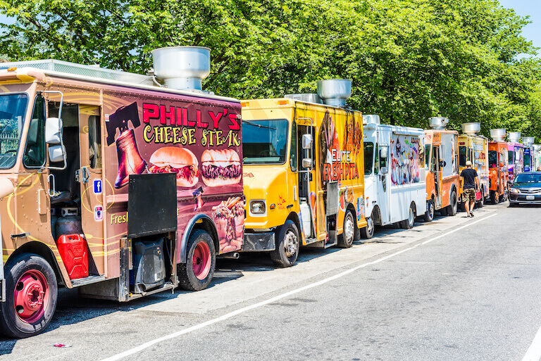 Food trucks on a street with cars driving by