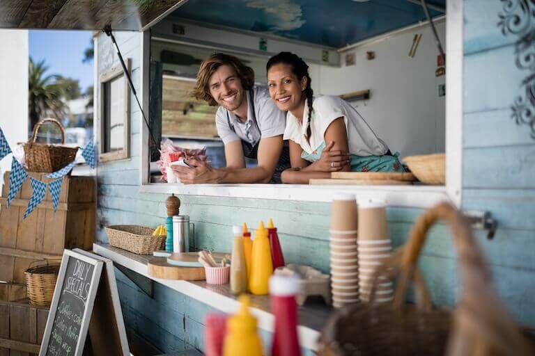 Two food truck employees leaning over the counter smiling