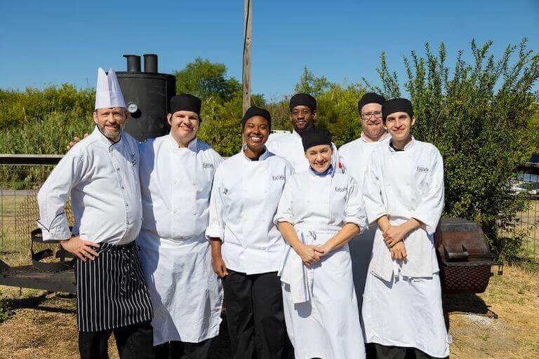 A group of culinary students posing for a photo outside in their uniforms