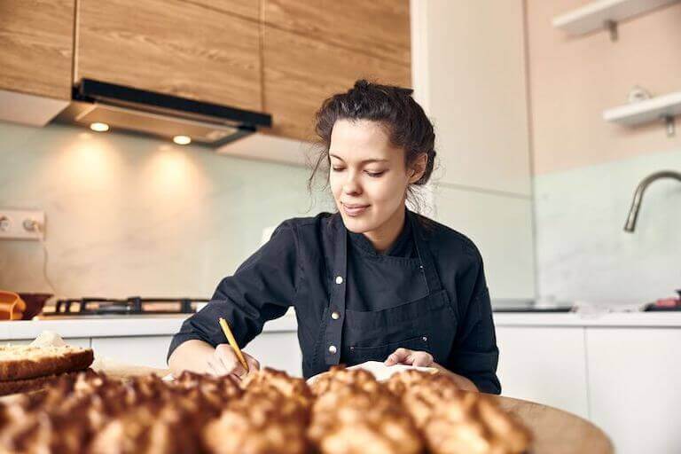 Chef wearing a black apron sitting at a table writing