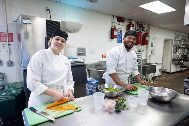 Escoffier students cutting carrots and potatoes in a kitchen