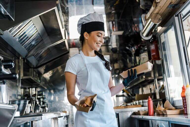 Happy female chef in a food truck holding cartons of food.