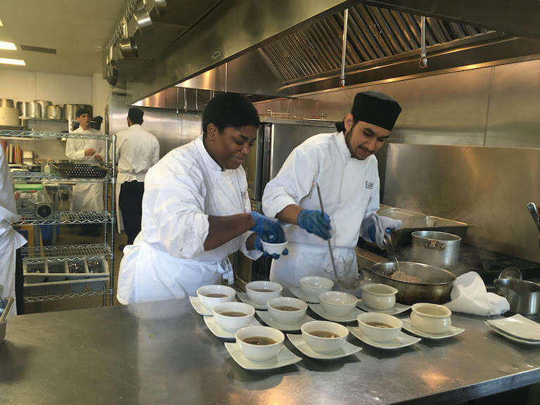 Oscar and another escoffier student put soup into bowls
