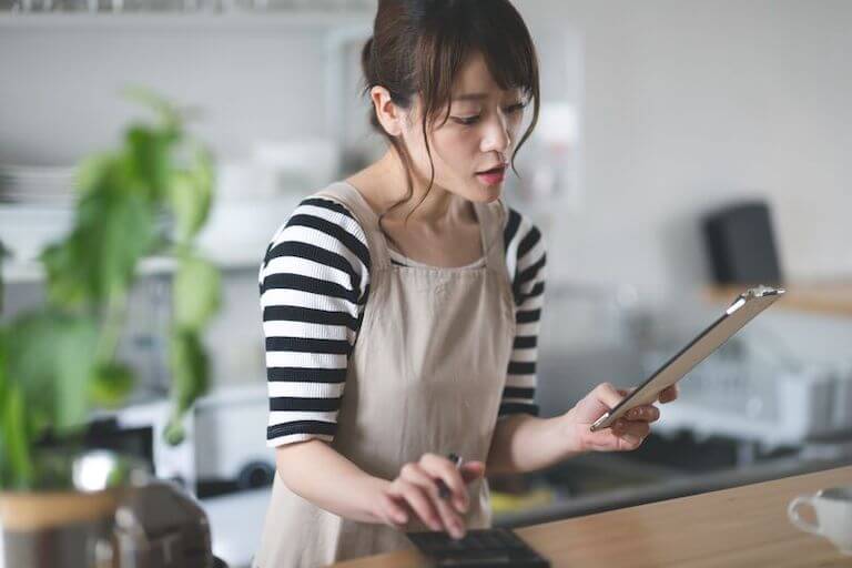 Person wearing a black and white striped shirt and a tan apron using a calculator