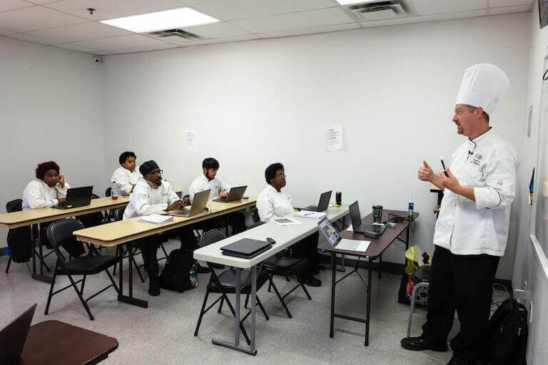 Students sitting in a class room while listening to a chef instructor
