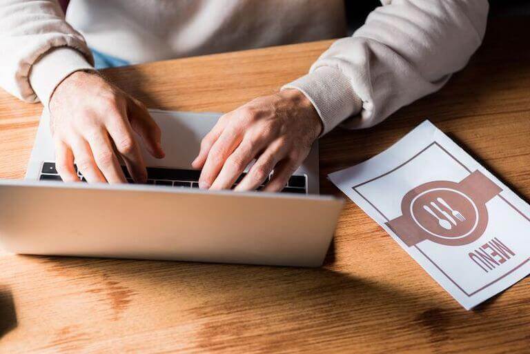 hands typing on a laptop with a menu sitting to the side