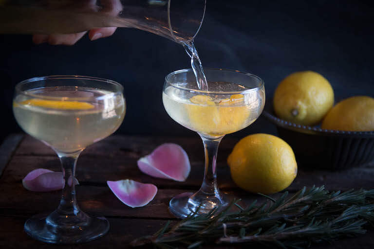 A drink being poured into a glass with a lemon and lemons in the background