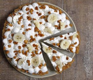 Banana Cream Pie Cheesecake with whipped cream and candied peanuts, sliced