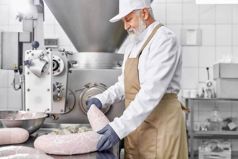 Butcher with a brown apron in an industrial kitchen making sausage