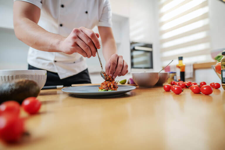 Chef standing in kitchen and putting cooked salmon on plate