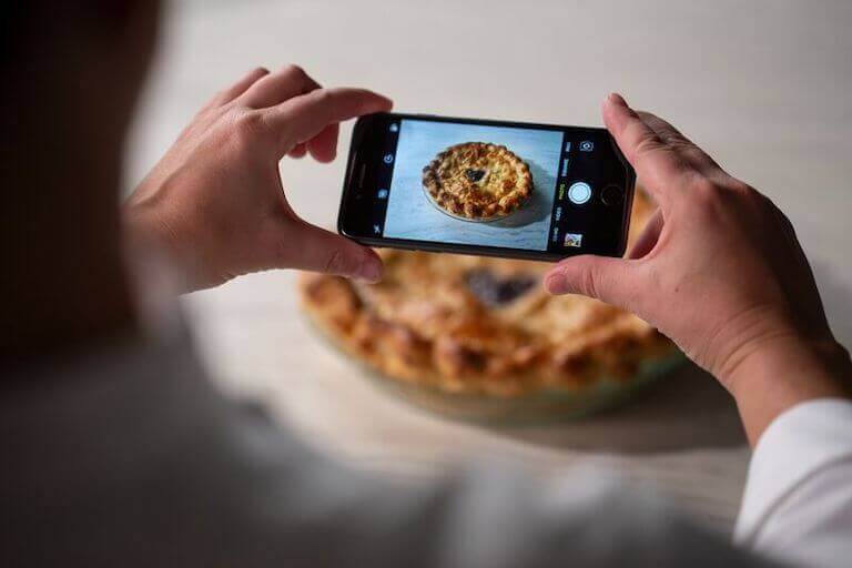 Close up of hands holding a phone to take a photo of a pie