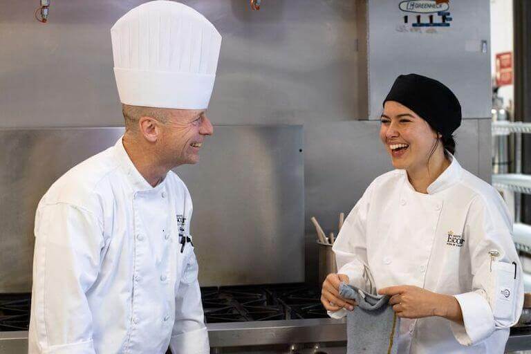 Culinary student and instructor smiling in a commercial kitchen