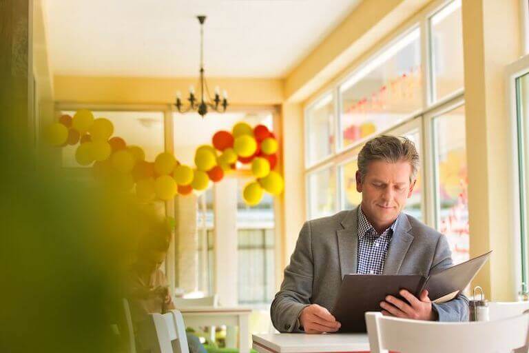Customer sitting at a table by a window with balloons while reading menu