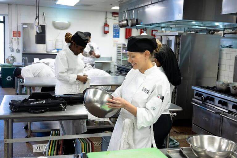 Escoffier student holding a silver bowl in a kitchen