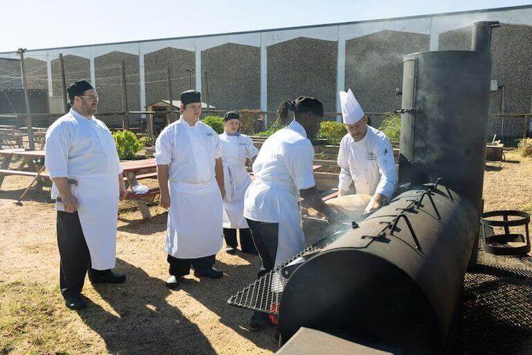 Escoffier students standing outside cooking on a large grill