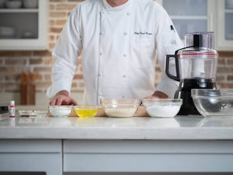 Flour, oil, and other macaron ingredients separated into bowls on a counter