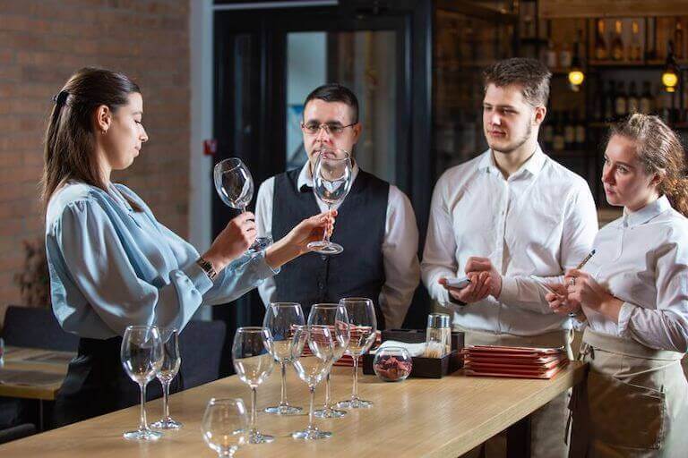 Manager showing staff different wine glasses while standing at the bar