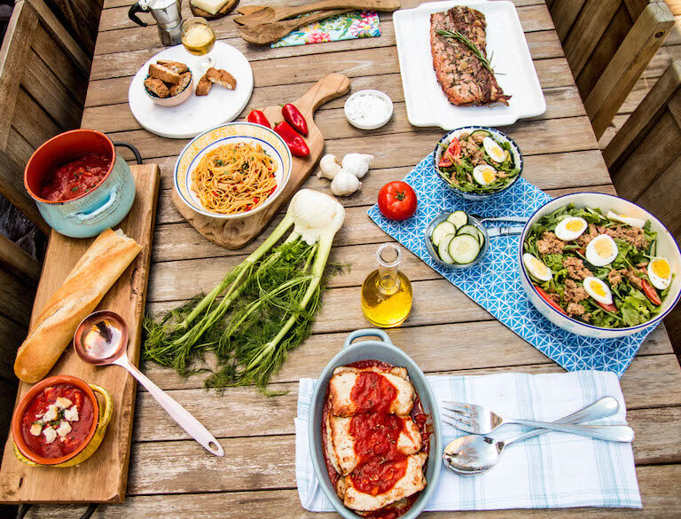 Pasta, salad, garlic, and other foods styled on a wooden table