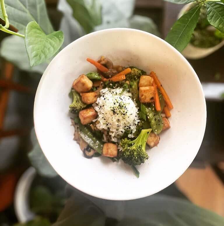 Plant based dish with rice, broccoli, and other vegetables in a white bowl
