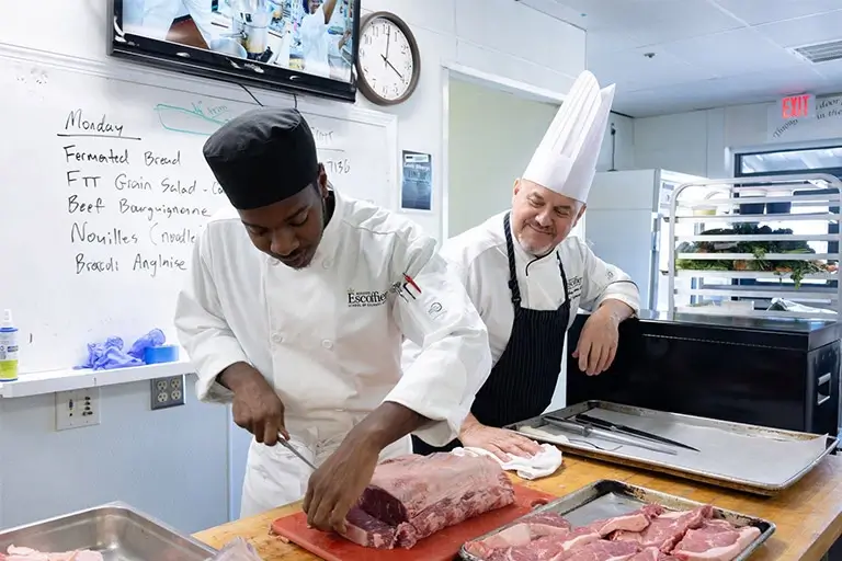 Culinary student learning butchering techniques at Escoffier Austin Campus with chef instructor observing