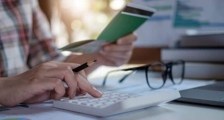 Close up of a hand typing numbers into a calculator and holding a pencil