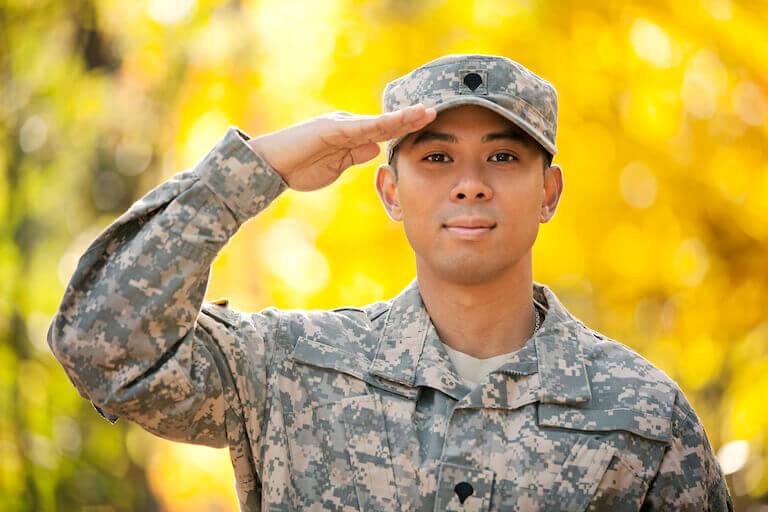 Man in a military uniform saluting while standing outside