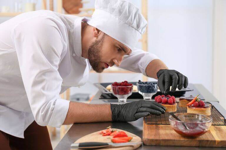 Pastry chef wearing black gloves adding berries to desserts