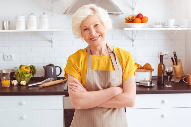 Smiling older woman wearing an apron with her arms crossed
