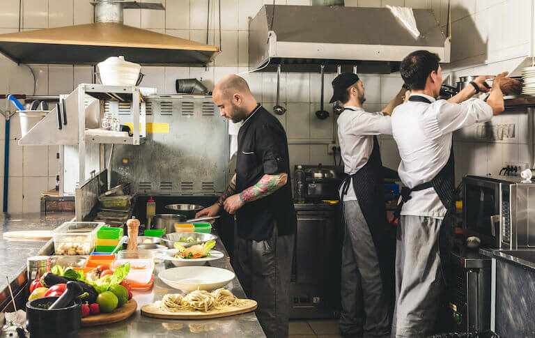 Three chefs in a restaurant kitchen preparing food