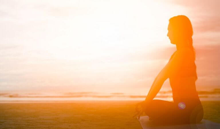 silhouette of a person practicing yoga outdoors on the beach in the morning