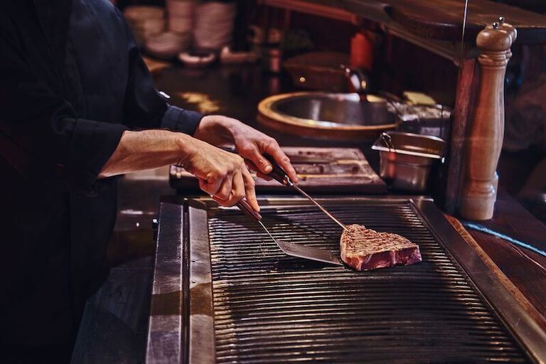 Chef cooking a piece of steak on a grill in a kitchen