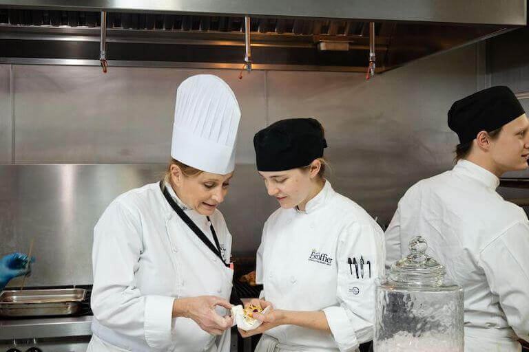 Escoffier student in a kitchen showing a chef instructor their work