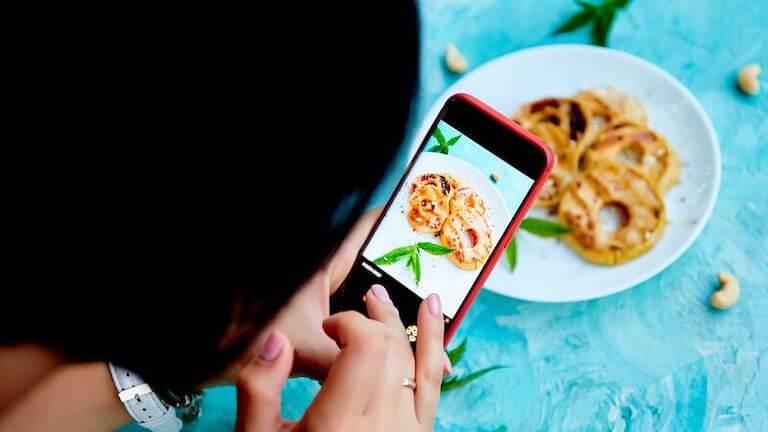 Influencer taking a photo of food on a blue table with their phone