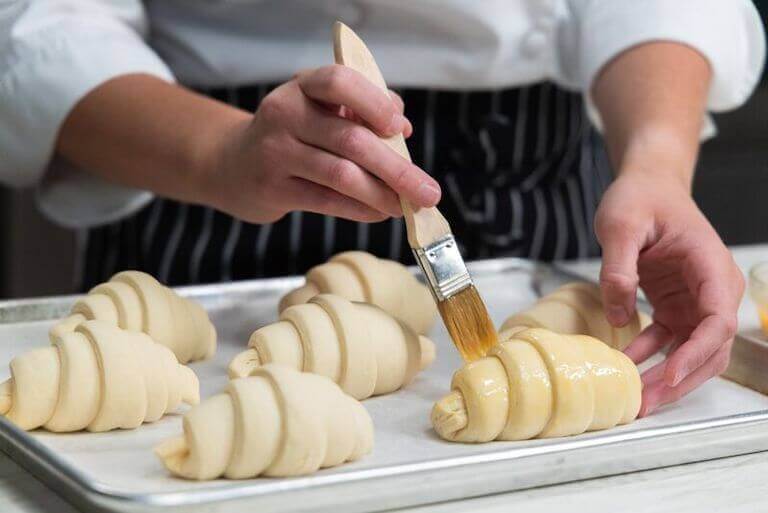 Chef brushing butter on a tray full of croissants