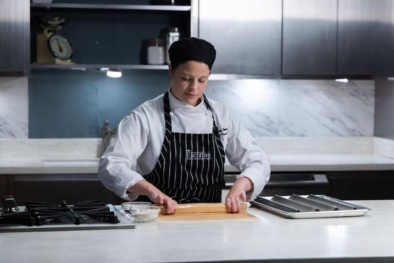 Escoffier student wearing a black and white apron making gluten free french bread in a kitchen