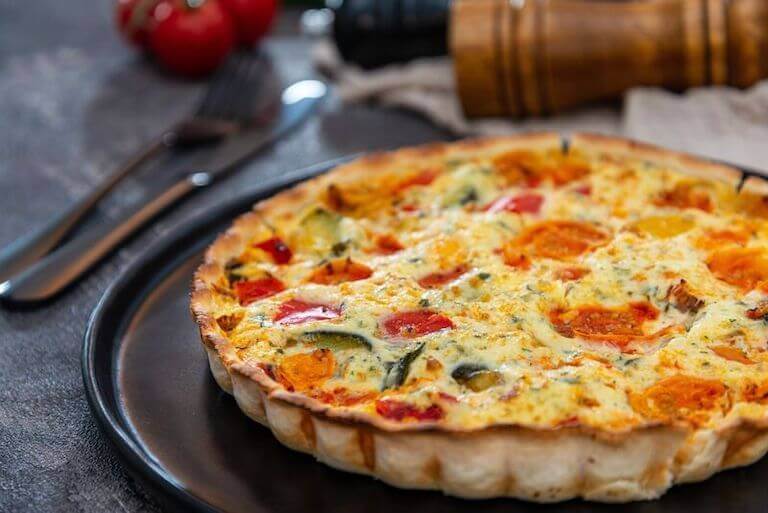 Quiche with cherry tomatoes, grilled peppers and courgettes on a black plate