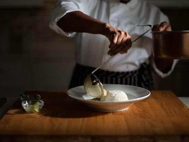 Chef ladling thai green curry on rice