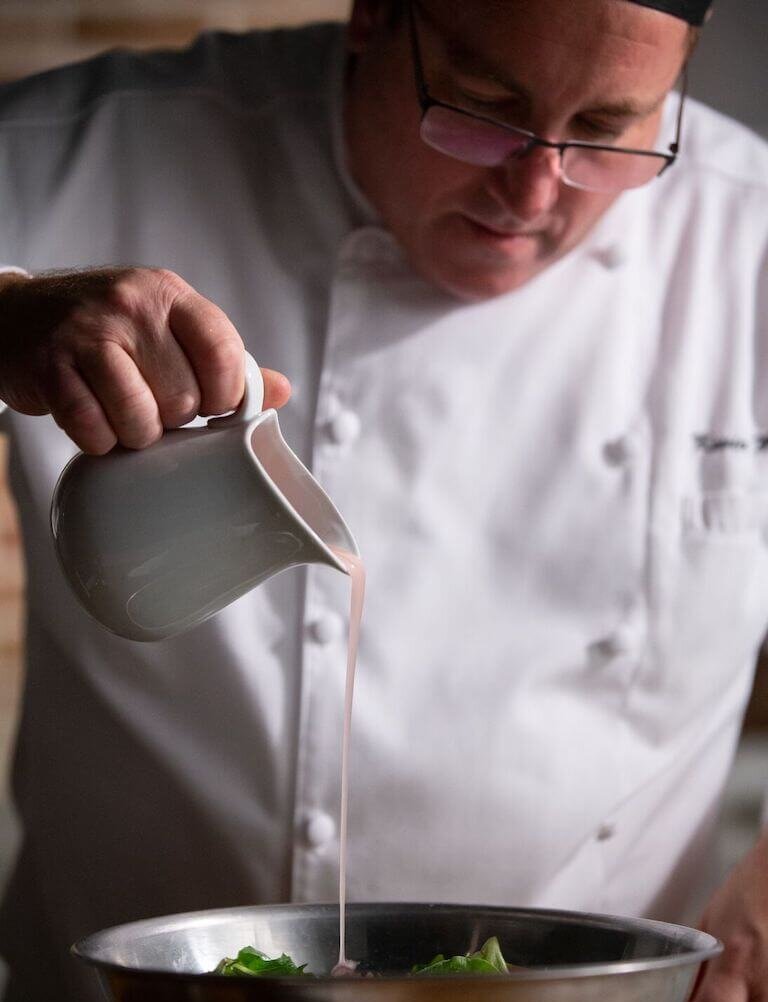Chef pouring vinaigrette onto salad in a bowl