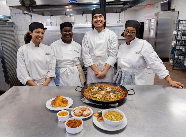 Culinary students smiling for a photo in the kitchen with a meal on a table