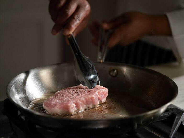 Tongs grabbing a pork chop in a pan