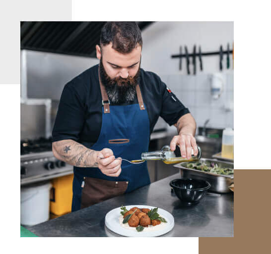 Chef working in restaurant preparing falafel over rice and placing olive oil with a spoon over the dish.