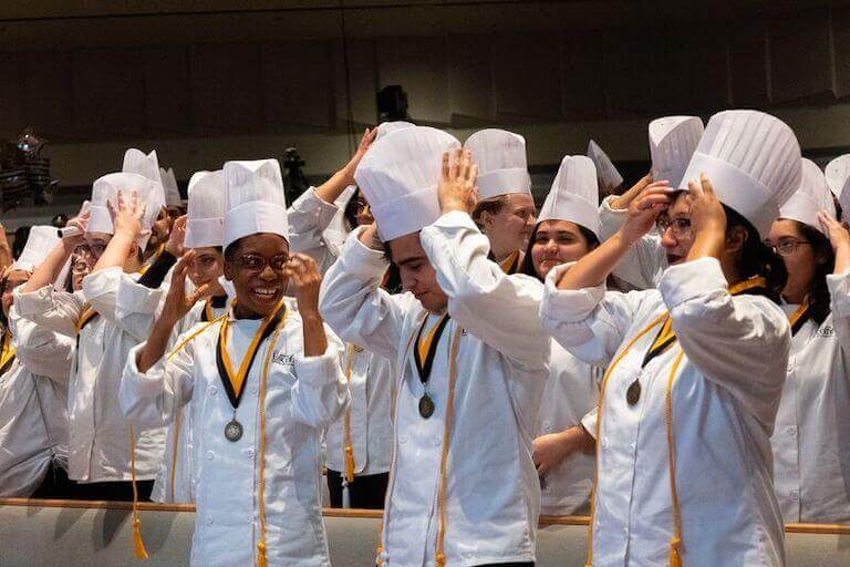 Escoffier students putting on their chef hats at graduation