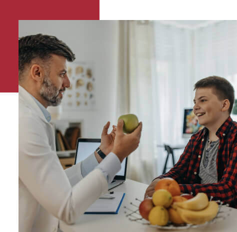 Nutritionist sitting at a desk with a young male patient holding an apple, showing how to help others build a positive relationship with food and diet