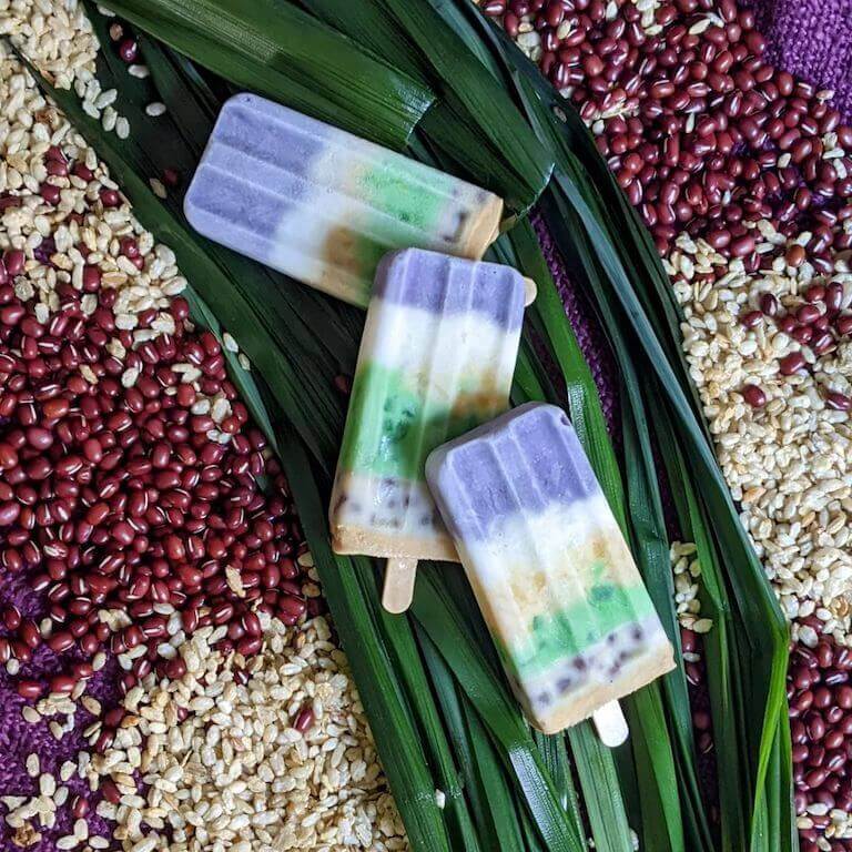 Colorful ube popsicles laying on a green background