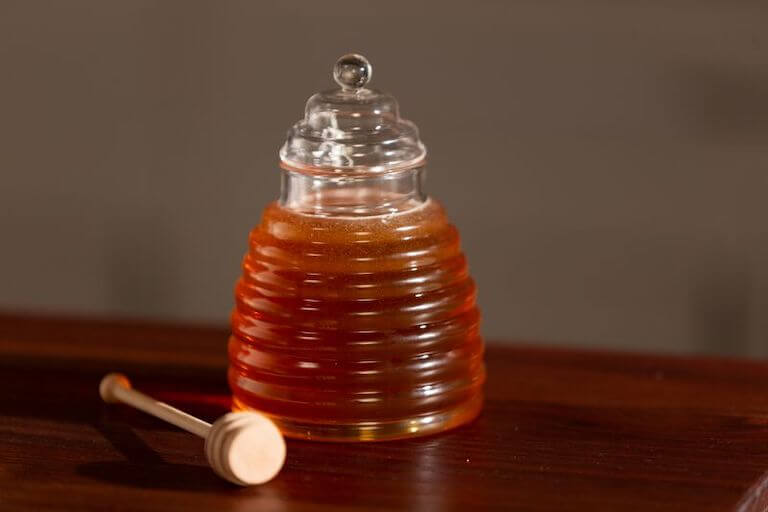 Glass jar with honey on a table next to a spoon