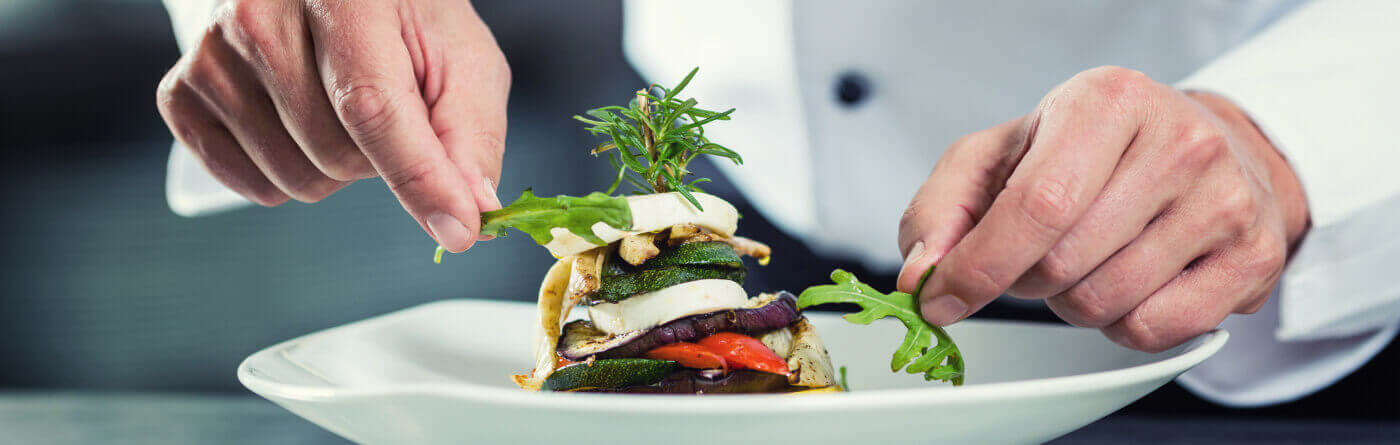 Close up of hands adding garnishes on a vegan dish, illustrating the latest plant-based methods and techniques