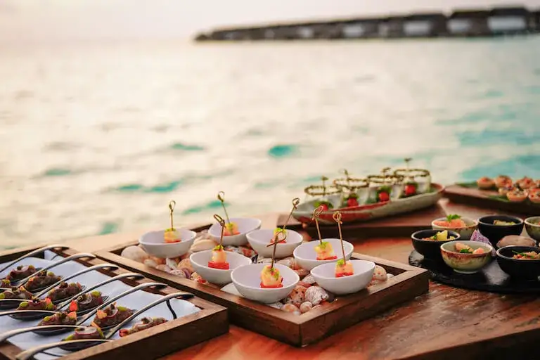 Plated canapes and small bites on wooden boards overlooking the ocean at sunset