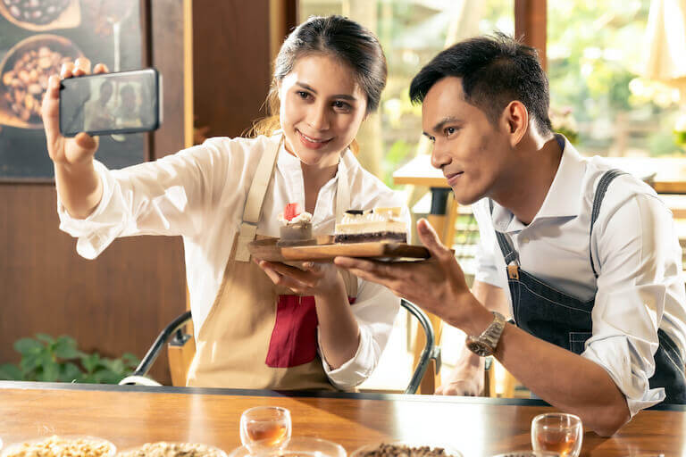 Two employees at a cafe taking a selfie with a pastry