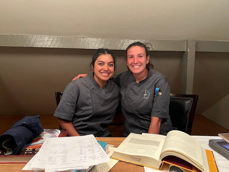 Chef Maggie and Araceli sitting at a desk with notes and books